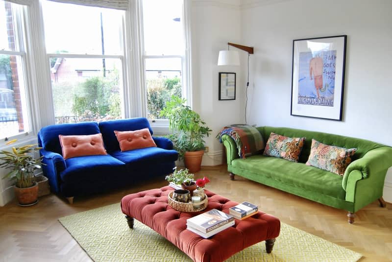 Living room with green velvet couch flanked by matching blue love seat and red ottoman.