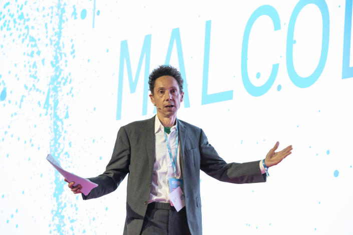 Malcolm Gladwell speaking in front of a large screen.