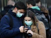 A couple wearing face masks to protect against the Coronavirus outbreak as they look at their photographs after visiting Buckingham Palace in London, Saturday, March 14, 2020. For most people, the new coronavirus causes only mild or moderate symptoms, such as fever and cough. For some, especially older adults and people with existing health problems, it can cause more severe illness, including pneumonia. (AP Photo/Frank Augstein)