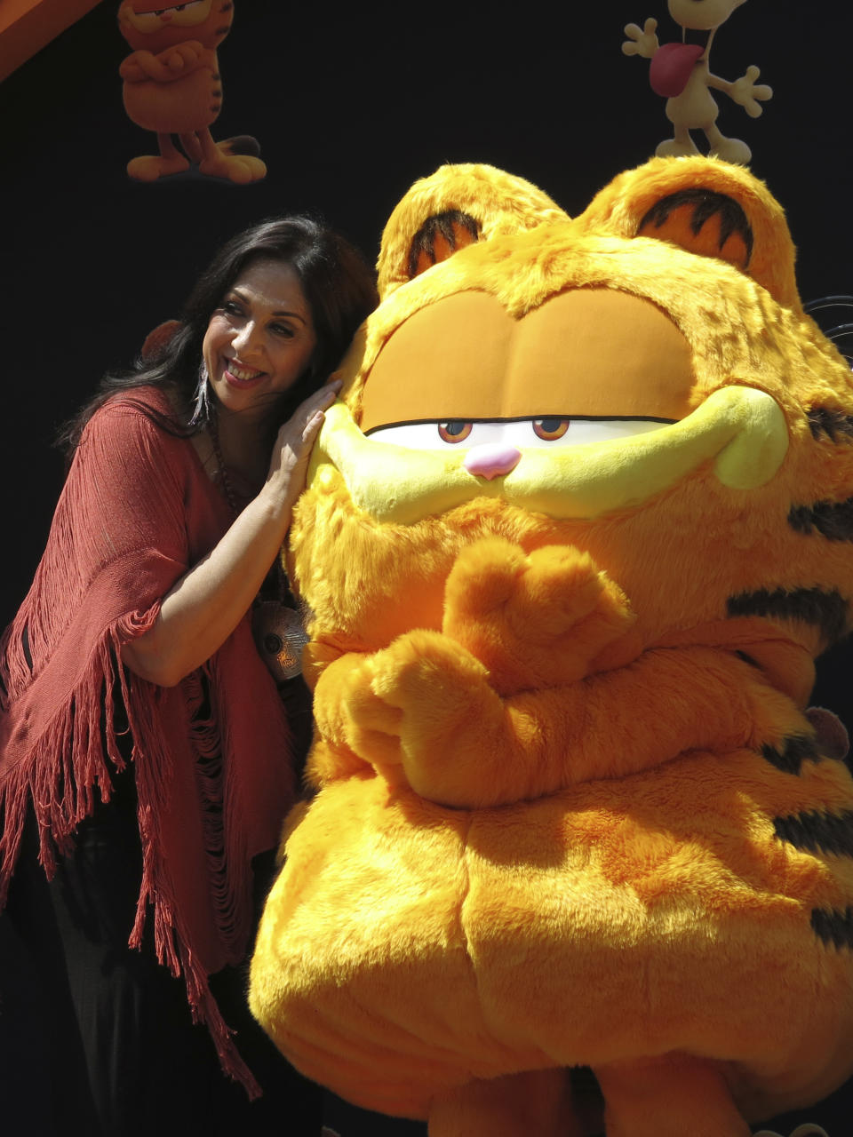 La actriz de doblaje Regina Orozco posa junto a un artista disfrazado del personaje Garfield en la alfombra naranja de la versión en español para Latinoamérica de "The Garfield Movie" en la Ciudad de México el domingo 28 de abril de 2024. (Foto AP/Berenice Bautista)