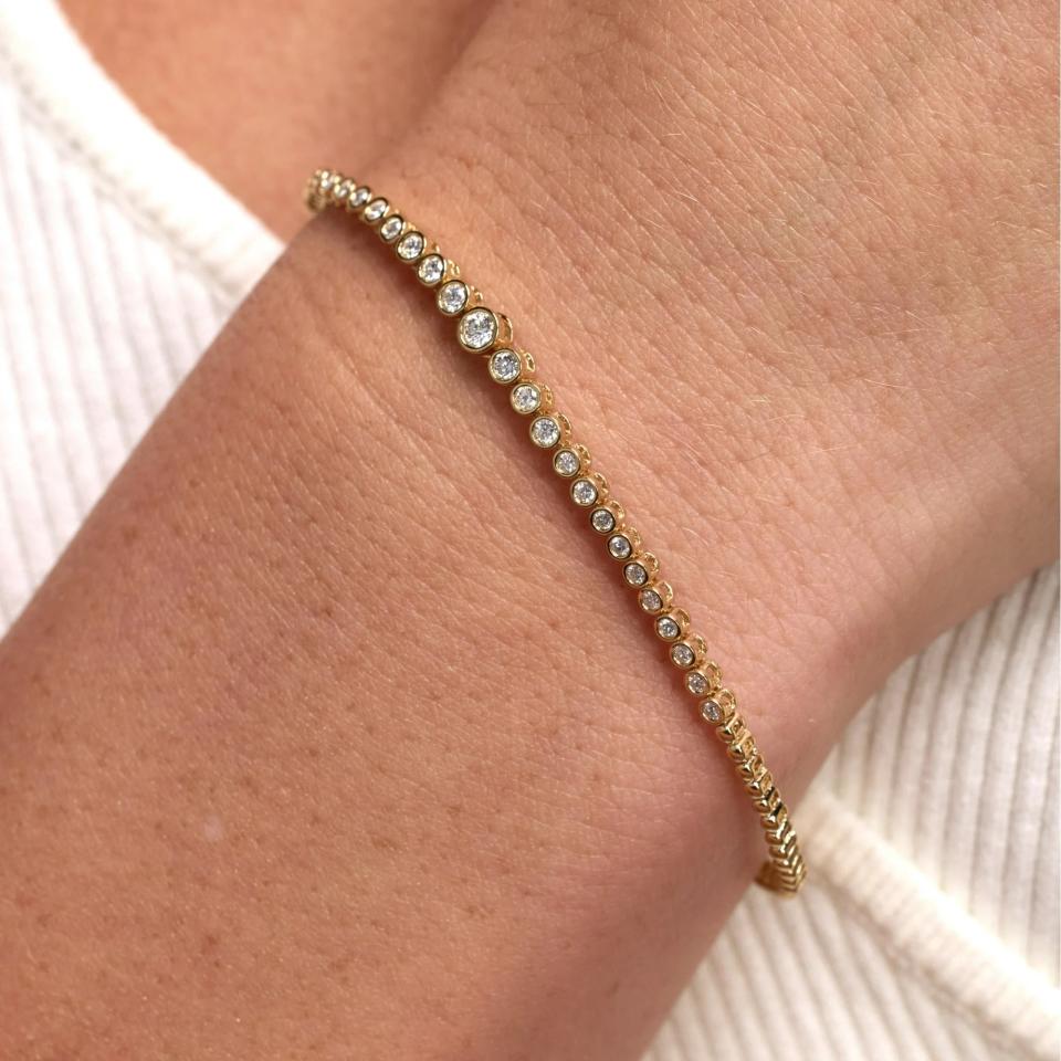 Wrist adorned with a delicate gold tennis bracelet featuring a single row of clear, round diamonds