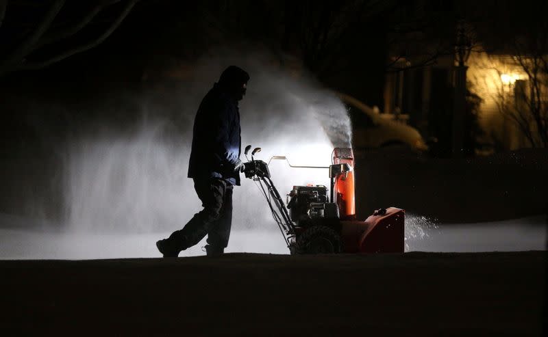 Roger Hake gets an assist from his truck lights as he clears snow from his driveway before the sun comes up in Webster