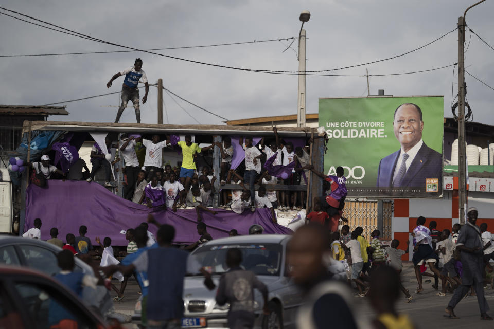 Supporters of the presidential candidate Kouadio Konan Bertin, ride a sound truck as they pass by an outdoor with a picture of the Ivory Coast President Alassane Ouattara during a final campaign rally in Abidjan, Ivory Coast, Thursday, Oct. 29, 2020. Bertin, known as KKB, has presented his candidacy as an independent candidate for the upcoming Oct. 31 election, and said he would not join the boycott proposed by two main opponents of Ivory Coast President Alassane Ouattara. (AP Photo/Leo Correa)