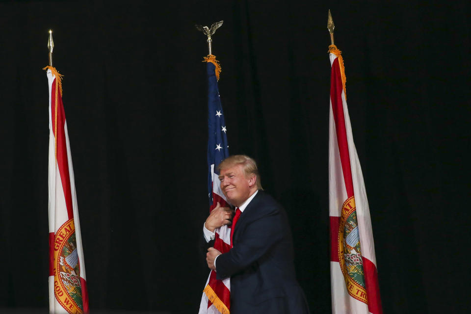 Donald Trump hugs the American Flag as he takes the stage during the rally at the MidFlorida Credit Union Amphitheatre in Tampa, Florida, on Monday, October 24, 2016. (Photo by Will Vragovic/Tampa Bay Times/Getty Images)