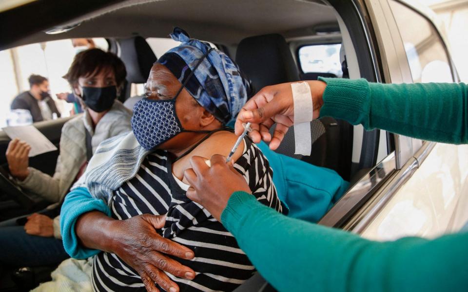 A woman receives a second dose of the Pfizer Covid-19 vaccine from a health worker while her employer looks on at the Zwartkops Raceway in Centurion, South Africa on 13 August 2021 - Phill Magakoe/AFP