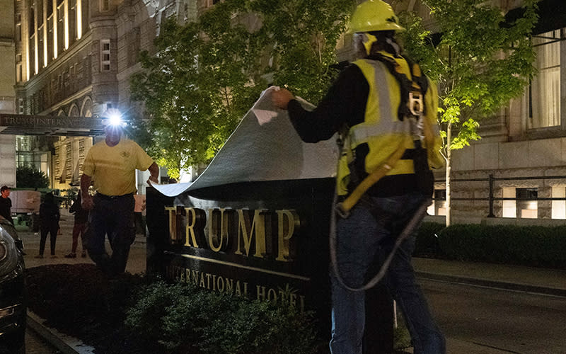 Two workers in hard hats cover a sign for the Trump International Hotel at night