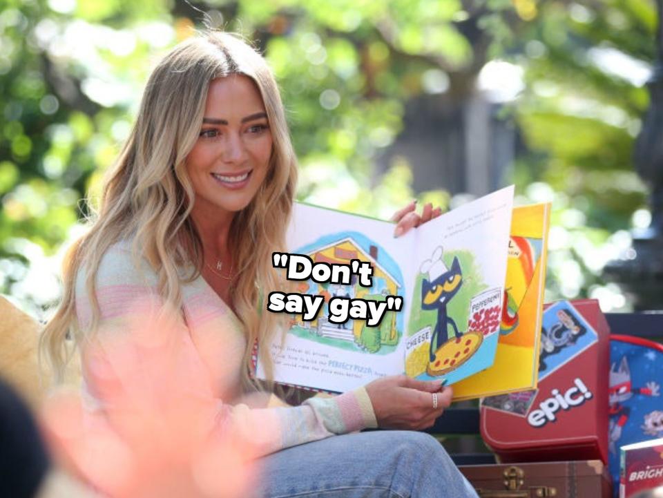 Hilary smiling and sitting with an open children's book with the caption "Don't say gay"