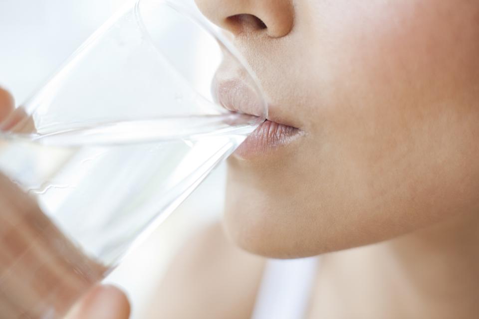 Close-up eines Mundes einer jungen Frau, die Wasser aus einem Glas trinkt.