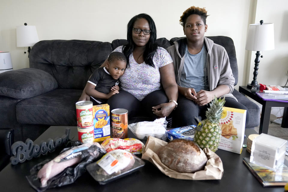 Briana Dominguez, center, sits with her sons, Noah Scott, 4, left, and Nehemiah Powell, 14, for a portrait inside their their Skokie, Ill., apartment with groceries she received at the Hillside Food Pantry. After her employer eliminated her job, the family is moving to Georgia where living costs are lower. (AP Photo/Charles Rex Arbogast)