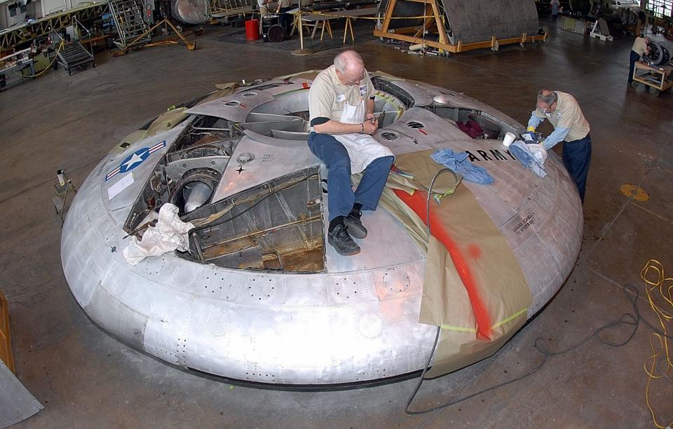 A photo of two men removing rivets from the Avrocar in the restoration hangar at the National Museum of the United States Air Force.