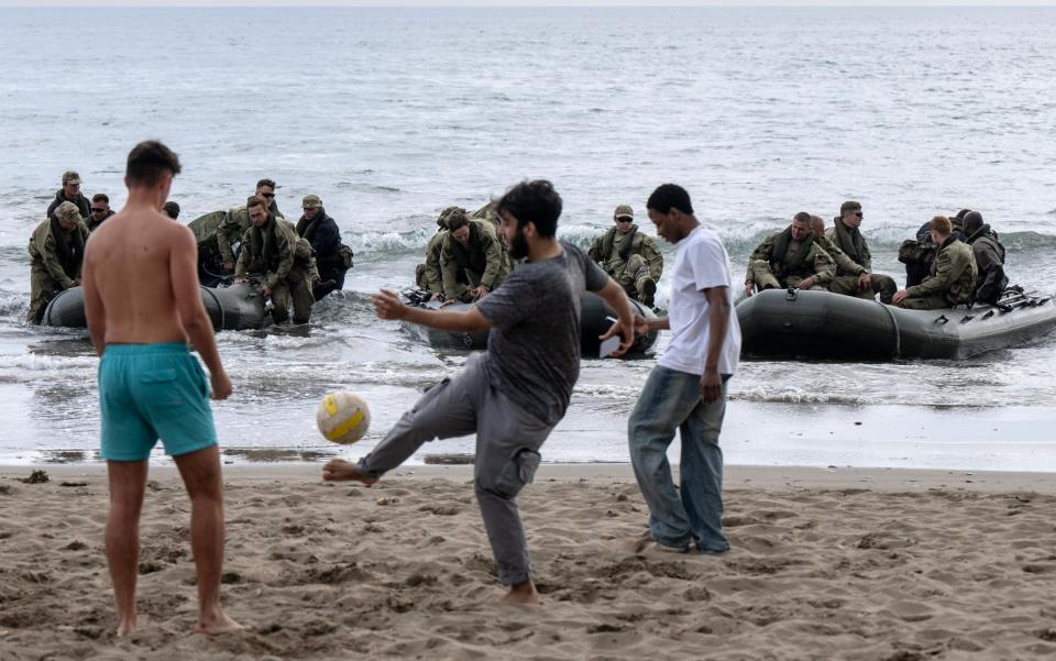 Beachgoers play football with marines in the background