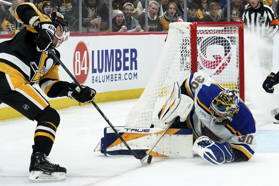 St. Louis Blues goaltender Joel Hofer (30) reaches for the puck against Pittsburgh Penguins' Reilly Smith, left, during the second period of an NHL hockey game Saturday, Dec. 30, 2023, in Pittsburgh. (AP Photo/Matt Freed)