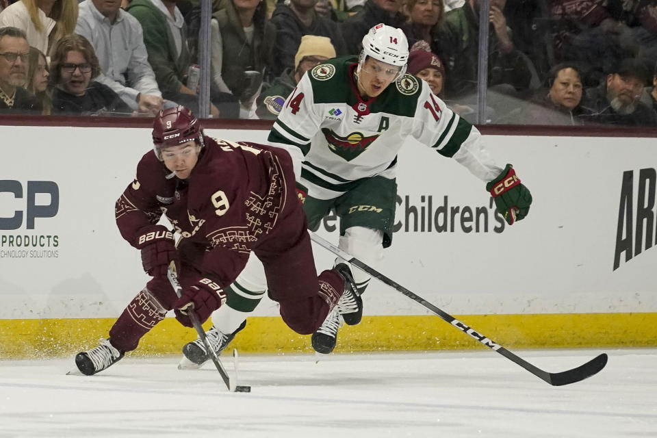 Arizona Coyotes' Clayton Keller (9) chases down the puck in front of Minnesota Wild's Joel Eriksson Ek (14) during the first period of an NHL hockey game Wednesday, Feb. 14, 2024, in Tempe, Ariz. (AP Photo/Darryl Webb)