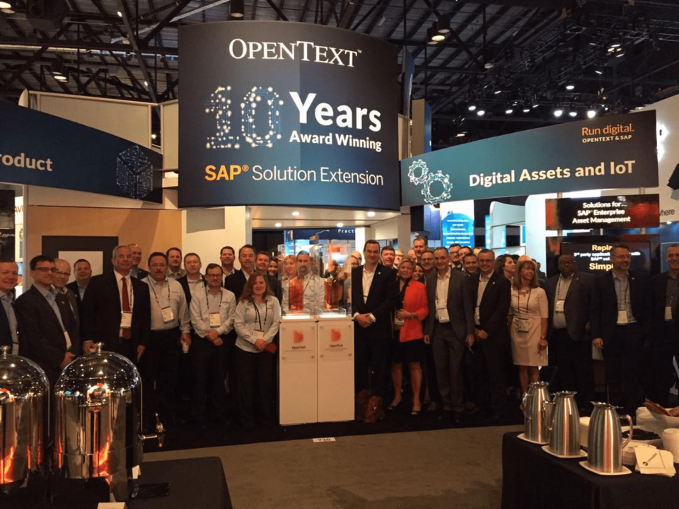 Conference hall with OpenText booth and about two dozen people lined up.