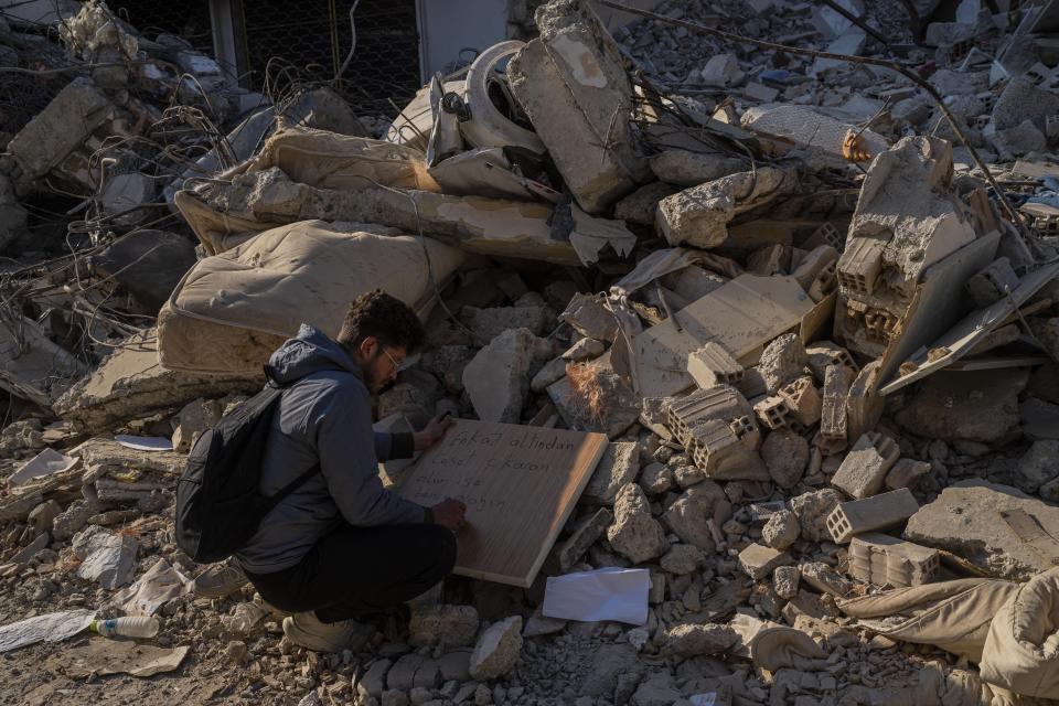 A man writes a text with contact details in case a body is retrieved under the rubble of a destroyed building in Antakya, southeastern Turkey, Monday, February 13, 2023. Thousands left homeless by a massive earthquake that struck Turkey and Syria a week ago packed into crowded tents or lined up in the streets Monday for hot meals as the desperate search for survivors entered what was likely its last hours. (AP Photo/Bernat Armangue)