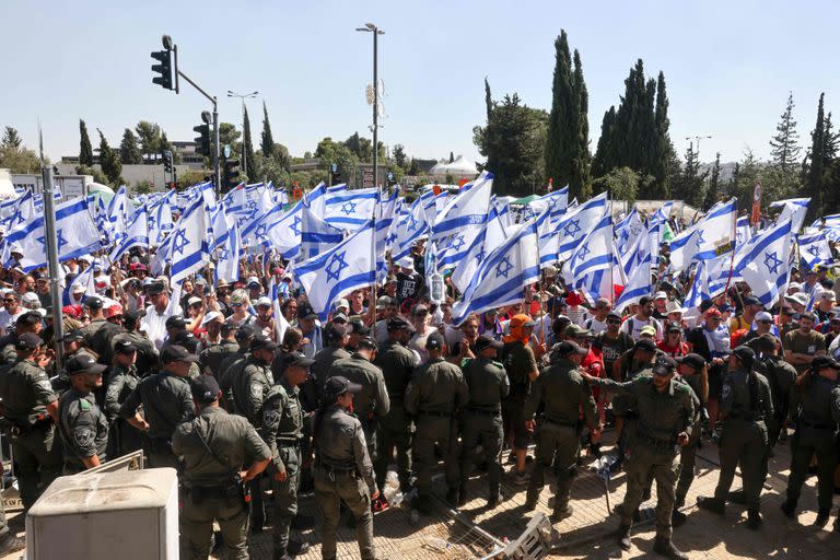 Las fuerzas de seguridad israelíes están en guardia mientras los manifestantes agitan la bandera nacional en la entrada del Knesset, el parlamento de Israel, en Jerusalén el 24 de julio de 2023. 