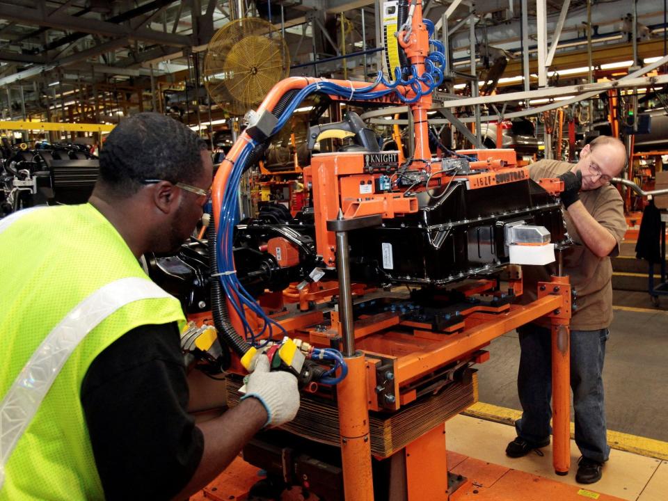 workers install a large vehicle battery onto an orange table