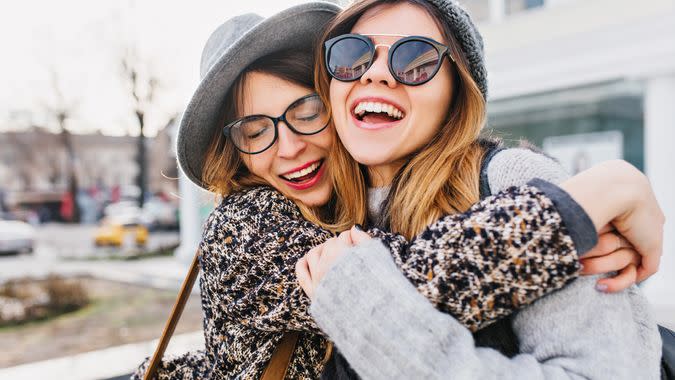 Happy brightful positive moments of two stylish girls hugging on street in city.