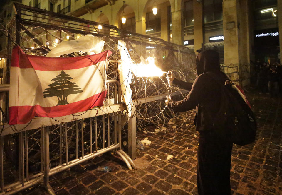 An anti-government protester uses an ignited aerosol can to shoot a stream of fire at the riot police who stand behind a barrier fence, during ongoing protests against the political elites who have ruled the country for decades, in Beirut, Lebanon, Sunday, Jan. 19, 2020. Lebanese security forces used tear gas, water cannons and rubber bullets in clashes with hundreds of anti-government protesters outside the country's Parliament on Sunday, as violence continued to escalate in a week of rioting in the capital. (AP Photo/Hassan Ammar)