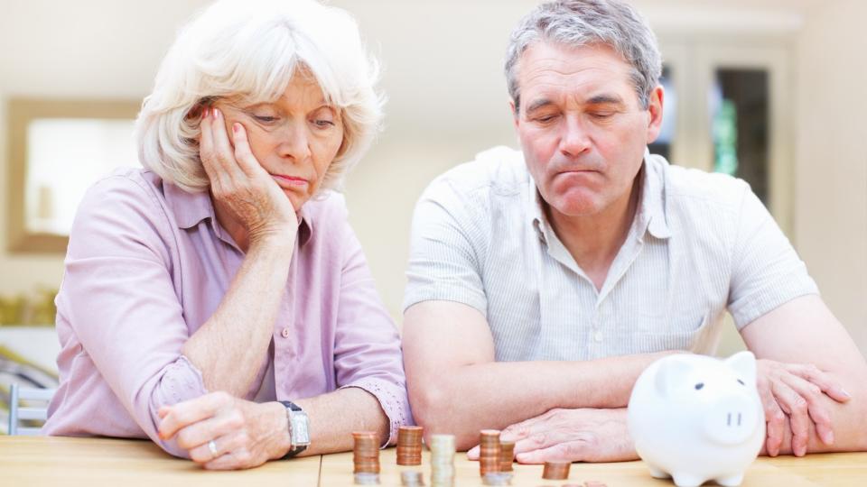  A worried senior couple sitting at a table looking at a piggy bank and several stacks of coins. 