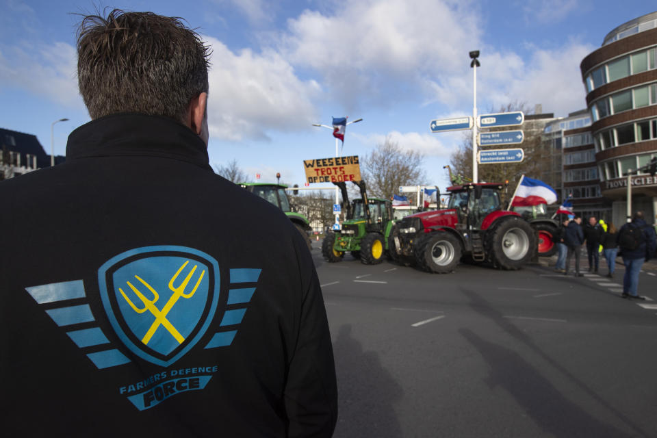 A farmer wearing the Farmers Defense Force jacket stands at an intersection blocked by tractors in The Hague, Netherlands, Wednesday, Feb. 19, 2020. Dutch farmers, some driving tractors, poured into The Hague on Wednesday to protest government moves to rein in carbon and nitrogen emissions to better fight climate change. (AP Photo/Peter Dejong)