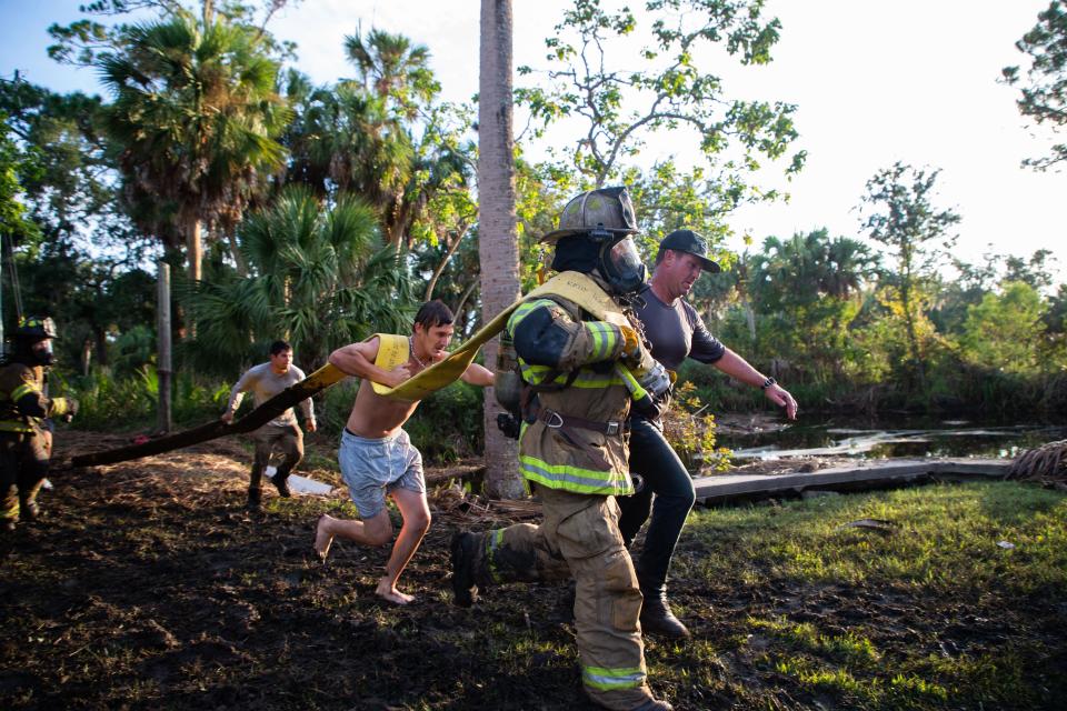 Neighbors, firefighters and others hustle down the limestone road with a firehouse as they attempt to tame a house fire in Suwannee, Fla. on Thursday, Aug. 31, 2023.