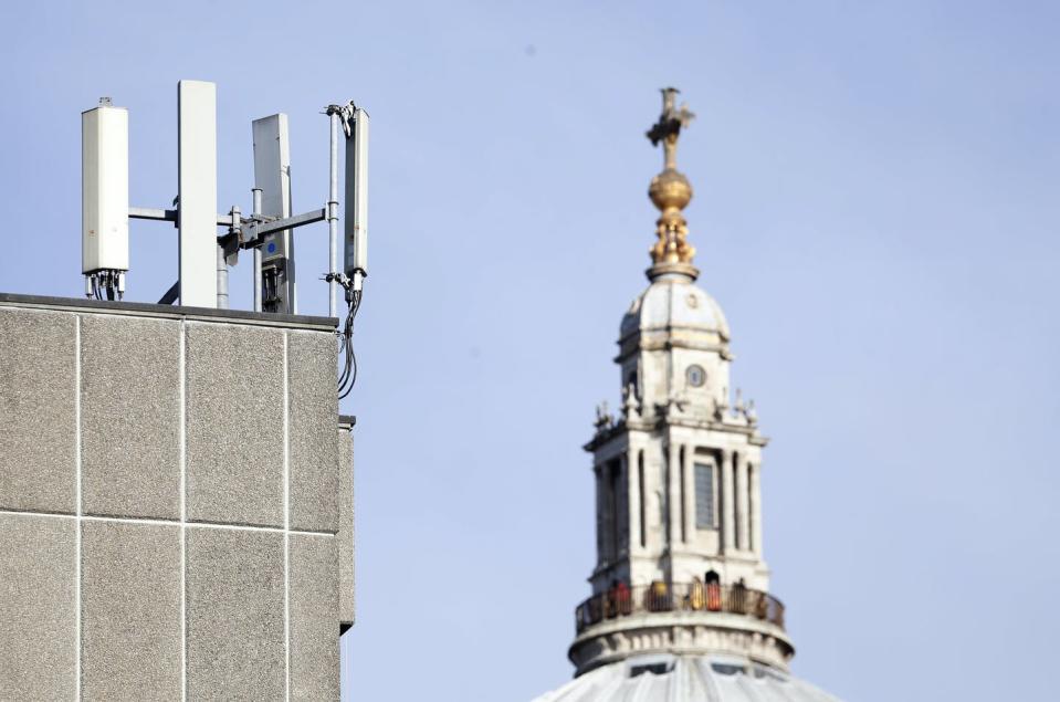 Four vertical rectangular devices mounted on the corner of a roof of a building with a church spire in the background