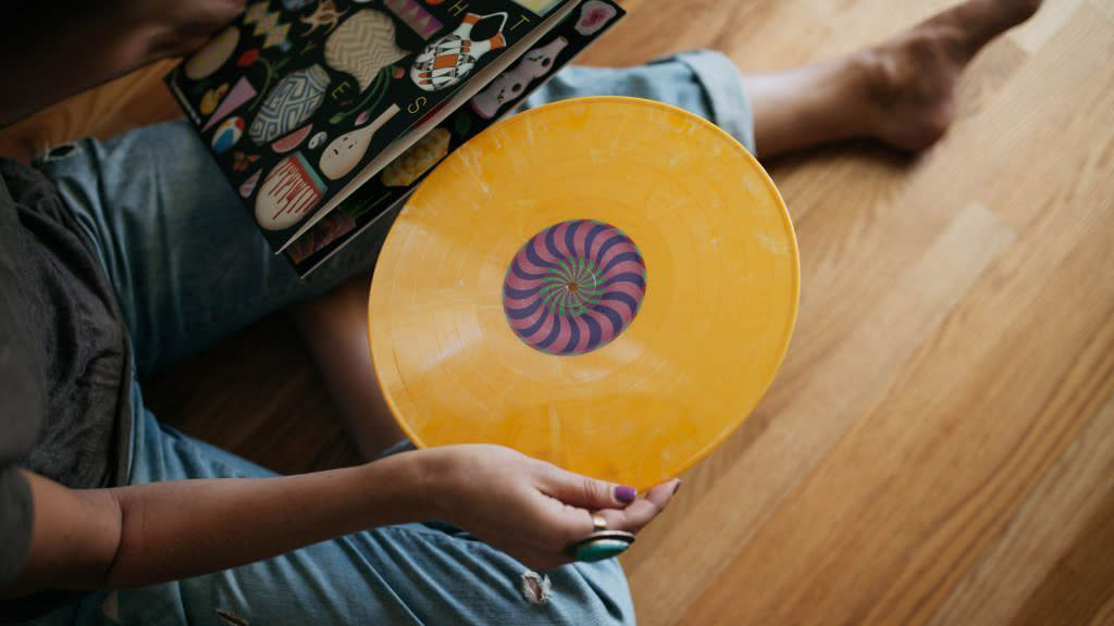  A yellow record being taken out of its sleeve by a man sitting on the floor. 