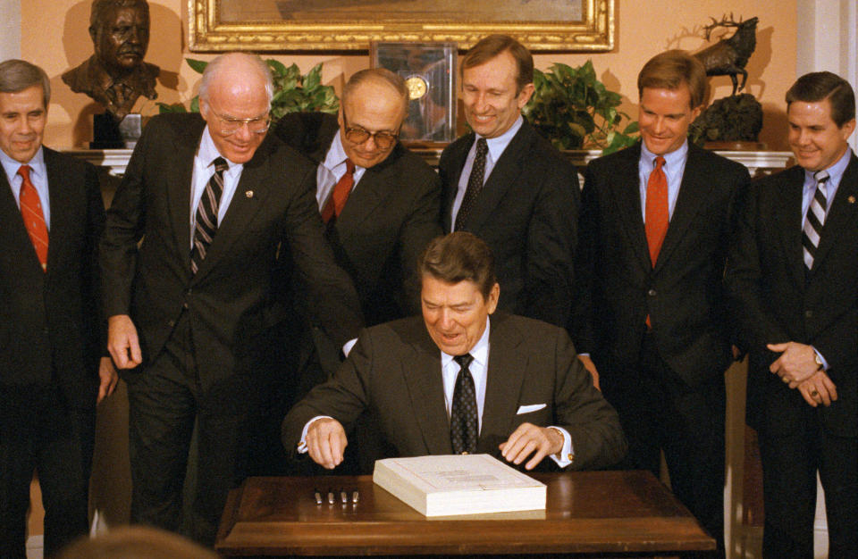 President Ronald Reagan reaches for a pen to sign legislation to bail out the farm credit system, providing the first federal aid to the nation's largest agriculture lender since the Great Depression. Behind Reagan, pushing in his chair for him, are (from left) Sen. Patrick Leahy (D-Vt.), Rep. John Dingell (D-Mich.) and Rep. James Jeffords (R-Vt.).