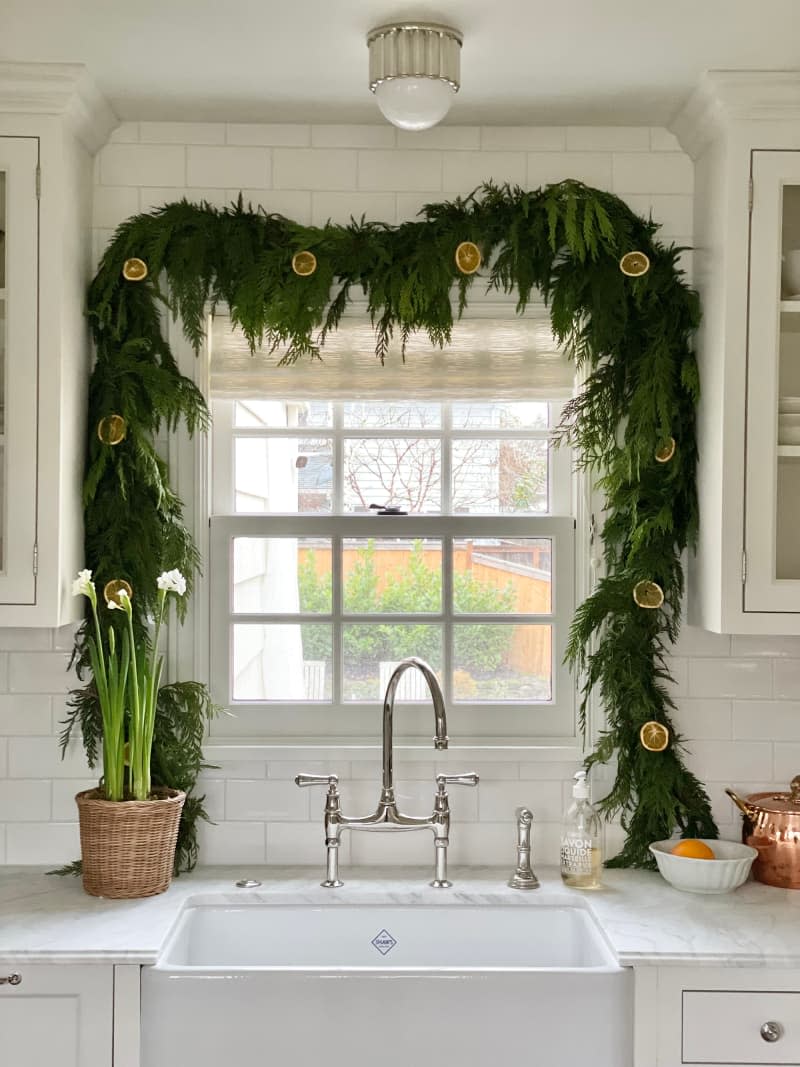 Kitchen window decorated with winter greenery and dried citrus fruit garland
