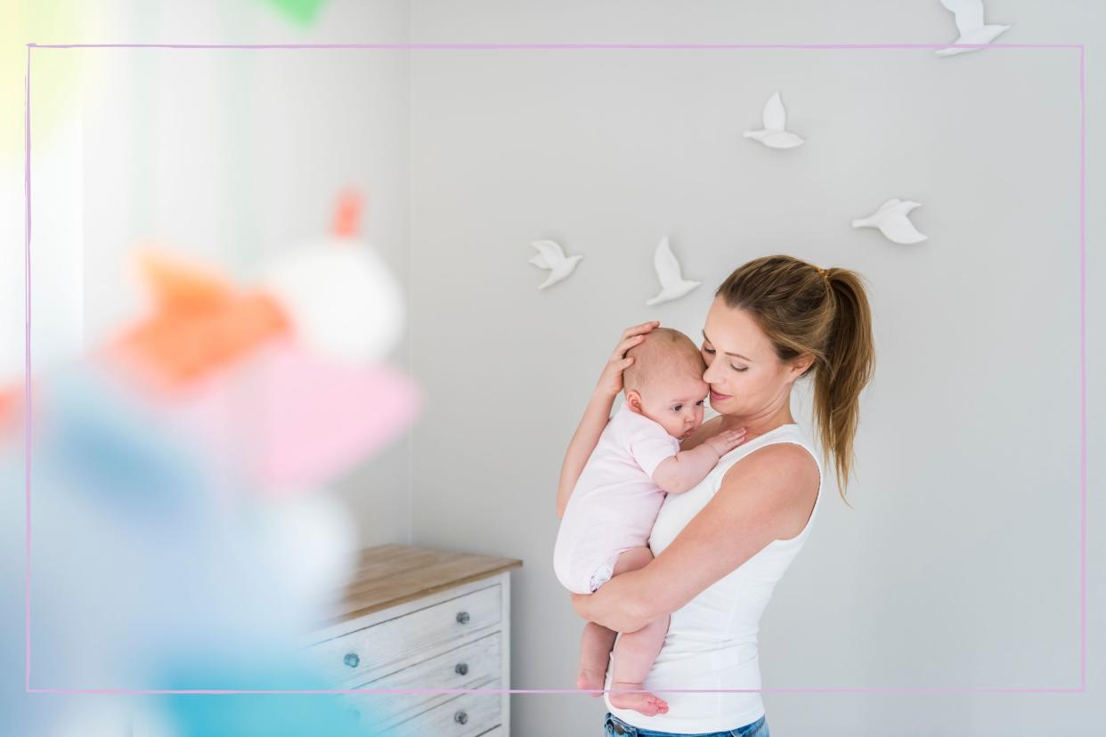  A woman carrying a baby in a nursery room with birds on the wall. 