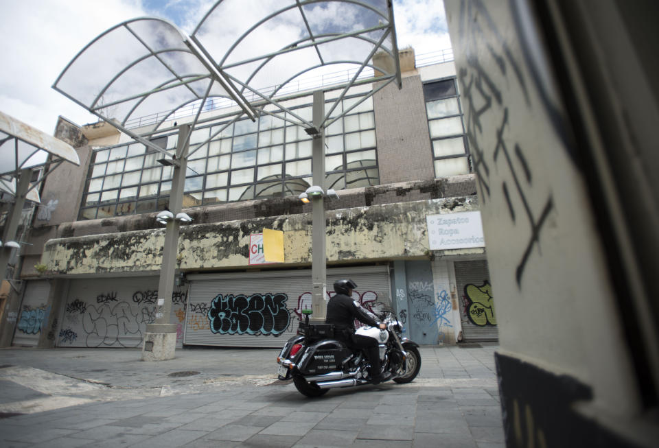 A municipal police officer drives past shuttered shops in the Paseo de Diego of San Juan, Puerto Rico, Wednesday, April 17, 2019. Many Puerto Ricans have left for Florida and New York. (AP Photo/Carlos Giusti)