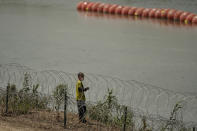 A migrant from Columbia walks along Concertina wire and a floating buoy barrier after crossing the Rio Grande from Mexico into the U.S., Monday, Aug. 21, 2023, in Eagle Pass, Texas. (AP Photo/Eric Gay)