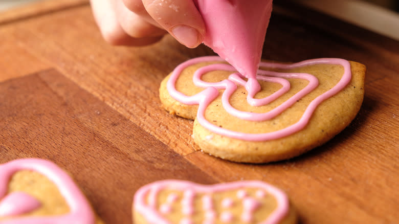 Person decorating heart-shaped sugar cookies