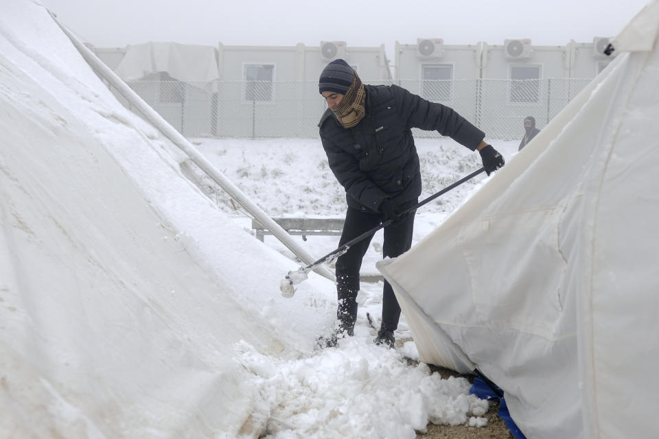 A migrant clears snow from makeshift tents at the Lipa camp, outside Bihac, Bosnia, Friday, Jan. 8, 2021. A fresh spate of snowy and very cold winter weather on has brought more misery for hundreds of migrants who have been stuck for days in a burnt out camp in northwest Bosnia waiting for heating and other facilities. (AP Photo/Kemal Softic)