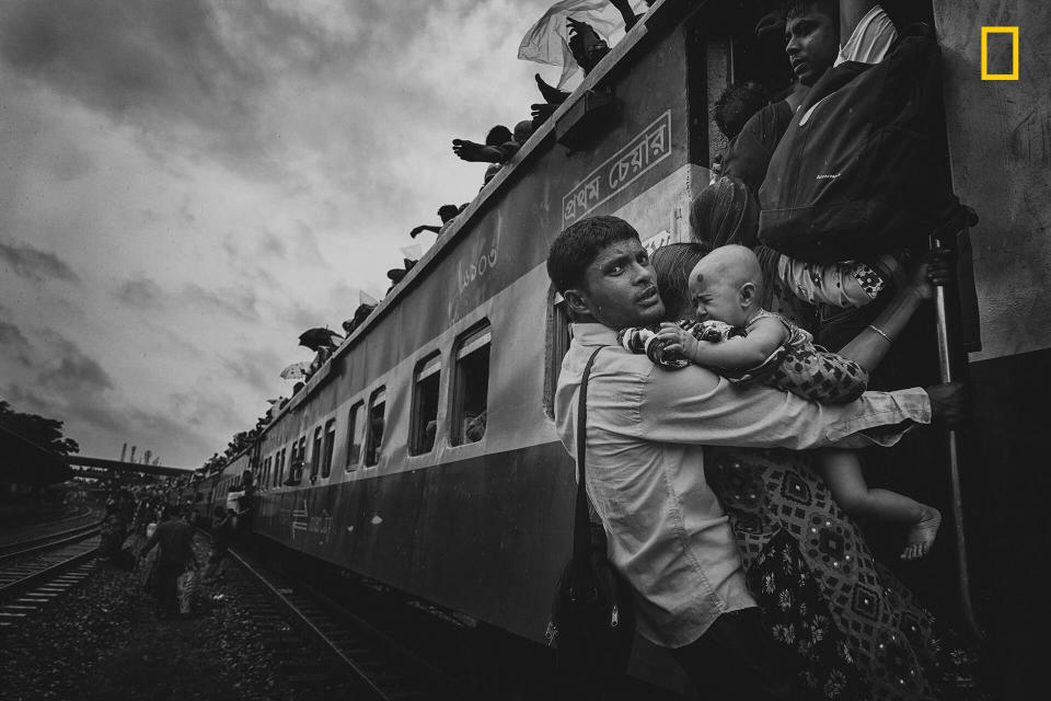 <strong>Third Place: "Challenging Journey"</strong><br /><br />"This photograph was taken from Dhaka's airport rail station during the Eid vacation. People were returning to their village homes to spend Eid with families, and the rush at the last hour was immense. One man caught my attention: He was dangling on a train's handle with his family, trying to get inside the train. At that time, rain started and the train began to slowly move. The family had tickets to board the train, but couldn&rsquo;t get to their seats. There are many people like him, who come to Dhaka for work &mdash; leaving their families and home villages &mdash; so when they get vacation, they don't want to miss the opportunity to spend time with dear ones, no matter what."