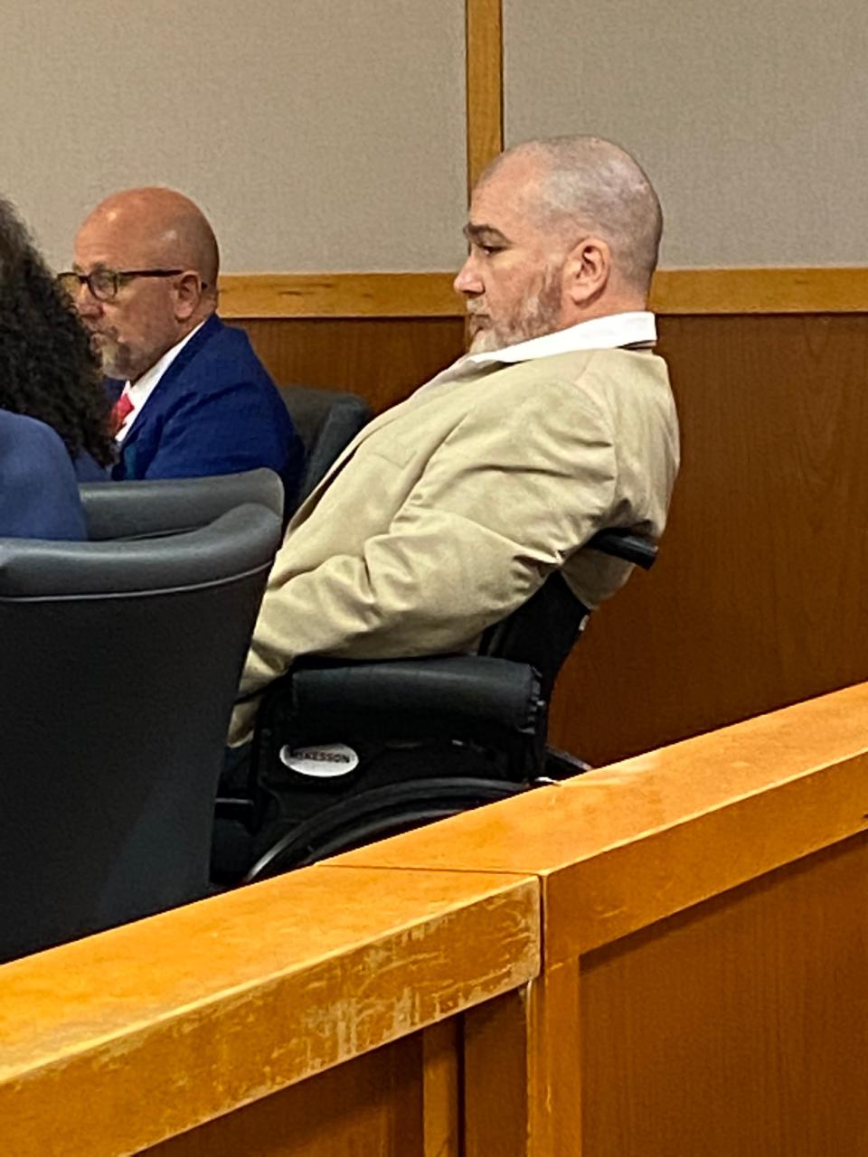 Jason Wheeler watches court proceedings from wheelchair at defense table.