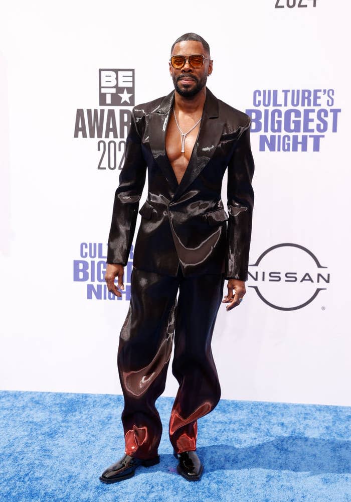 Colman Domingo at the BET Awards 2021, wearing a shiny black suit with a deep V-neck and wide-legged pants on the blue carpet