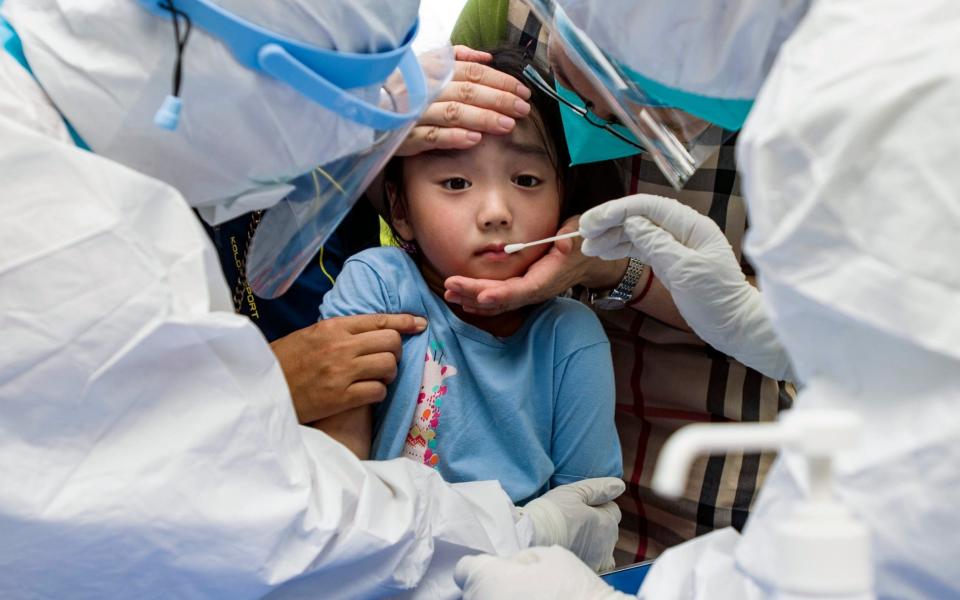 A child reacts to a throat swab during mass testing for COVID-19 in Wuhan - China Topix/AP