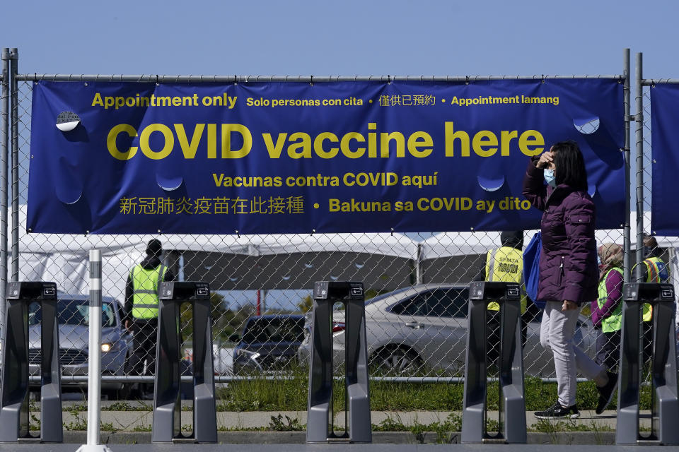 A pedestrian wears a face mask while walking past a sign at a vaccination center at City College of San Francisco during the coronavirus pandemic in San Francisco, Thursday, March 25, 2021. (AP Photo/Jeff Chiu)