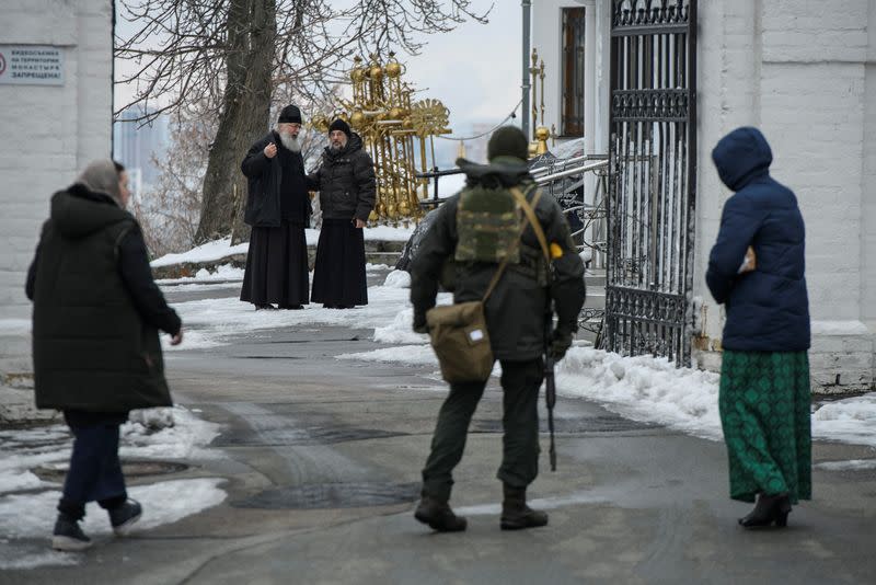 Orthodox priests look at a member of Ukrainian law enforcement at a compound of the Kyiv Pechersk Lavra monastery in Kyiv