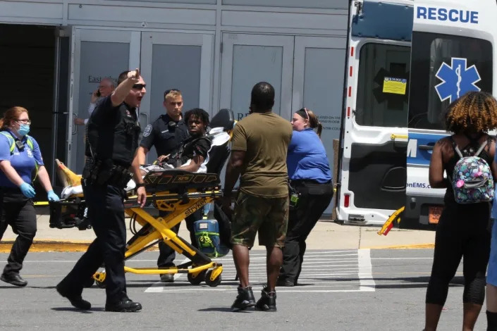 A Gastonia Police officer at the scene of a mass shooting at Eastridge Mall on Friday, June 10, 2022. Paramedics remove one of the injured in the background