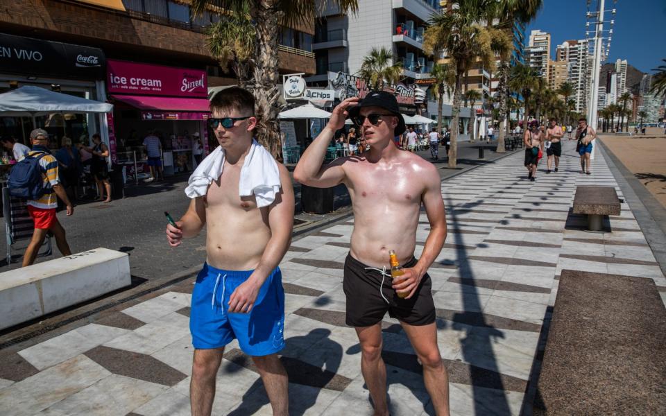 Tourists stroll shirtless on the beach promenade of Levante beach as a heatwave sweeps across Spain - Getty Images