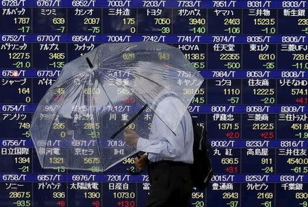 A man holding an umbrella walks in front of an electronic stock quotation board outside a brokerage in Tokyo September 8, 2015. REUTERS/Issei Kato