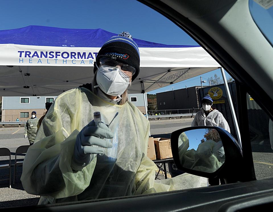 Ana Paula, a technician with Transformative Health, provides COVID-19 testing at a drive-thru site in the Ashland MBTA Commuter Rail inbound parking lot, Oct. 18, 2021.