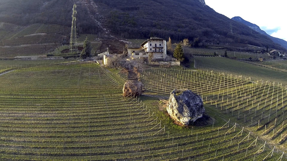 In this photo provided by Tareom.com Thursday, Jan. 30, 2014, and taken on Jan. 23, 2014, a huge boulder is seen after it missed a farm house by less than a meter, destroying the barn, and stopped in the vineyard, while a second giant boulder, which detached during the same landslide on Jan. 21, 2014, stopped next to the house, in Ronchi di Termeno, in Northern Italy. According to reports, the Trebo family living there was unharmed in the landslide. The boulder in foreground is from a much older landslide. (AP Photo/Markus Hell, Tareom.com, ho)