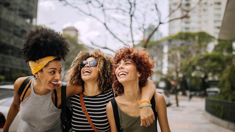 Tres amigas en la calle, abrazadas y riéndose.