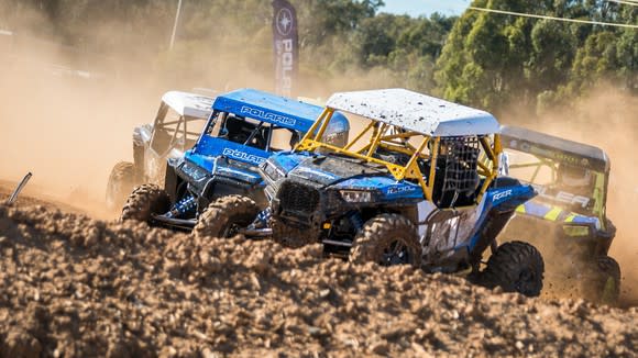 Several off-road vehicles with Polaris logos on a muddy track racing.