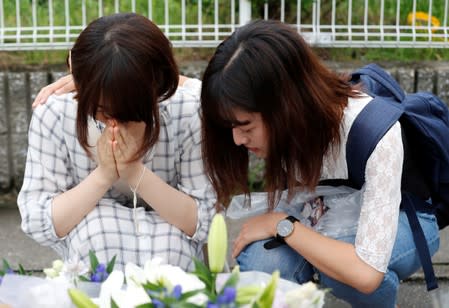 Women pray in front of a row bouquets placed out for victims of the torched Kyoto Animation building in Kyoto