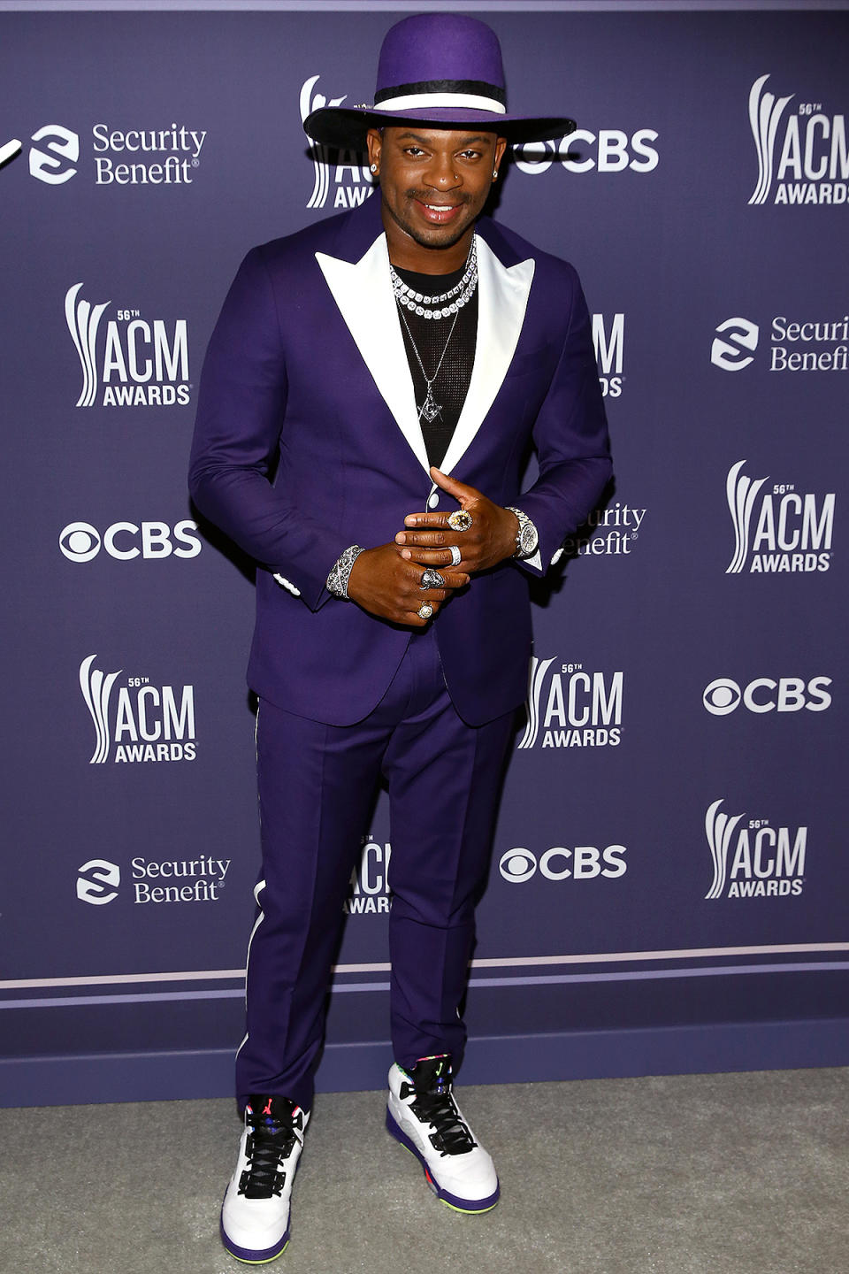 <p>teams his bright purple tux with white accents with a matching hat, double-strand necklace and statement rings. </p>